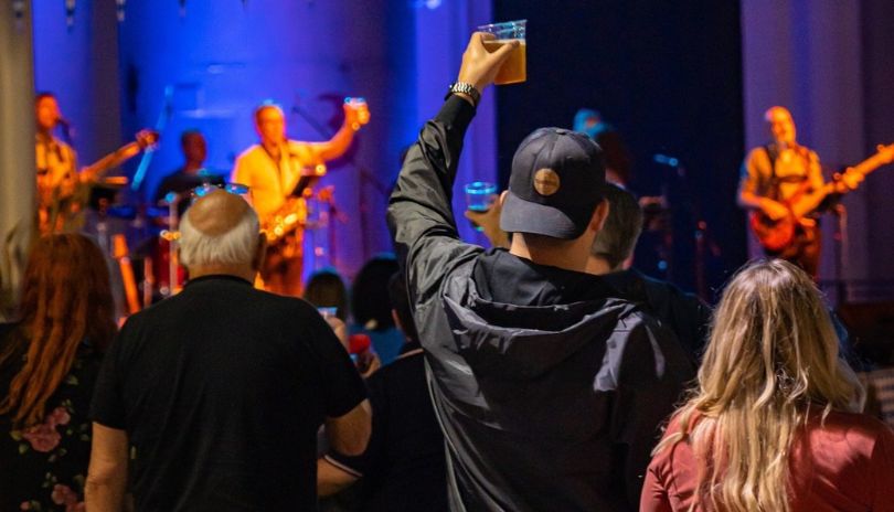 Band performing to an energetic crowd at 100 Kellogg Lane, with beer kegs behind them